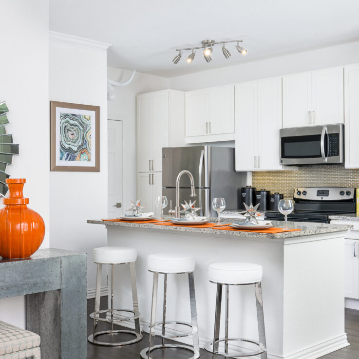 Kitchen with white cabinets, white barstools, marble countertops, and stainless steel appliances